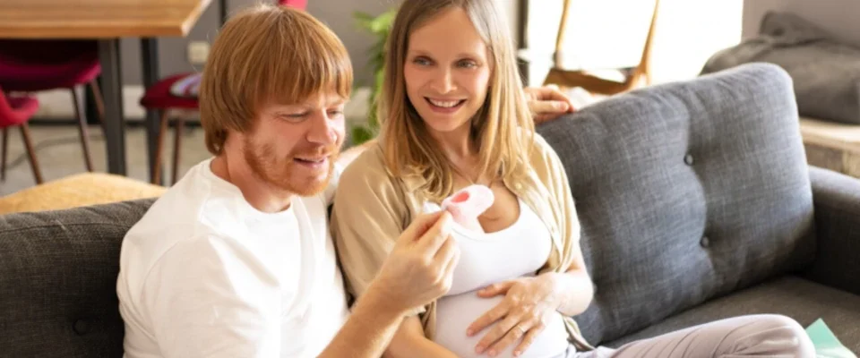 Happy pregnant couple checking baby clothes in living room