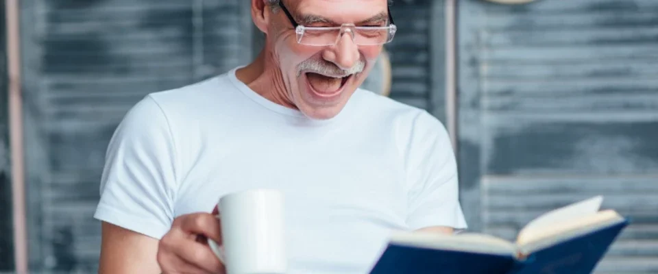 Portrait of eldery man sitting on bed, holding book, smiling happily