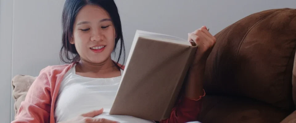 Young asian pregnant woman read a book for baby in belly